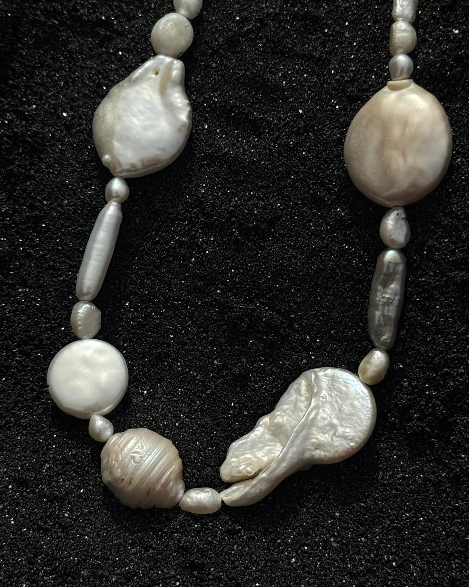 A strand of baroque pearls on black sand