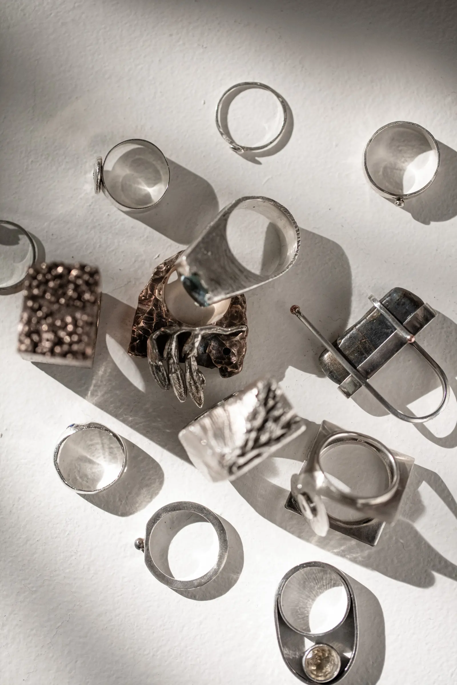 A hand reaching up wearing a ring; custom silver pieces on a table